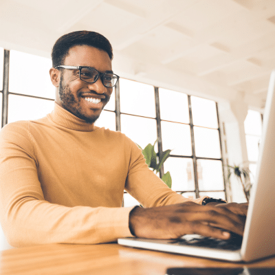 Man in yellow shirt smiling while he works on a laptop computer, representing new website