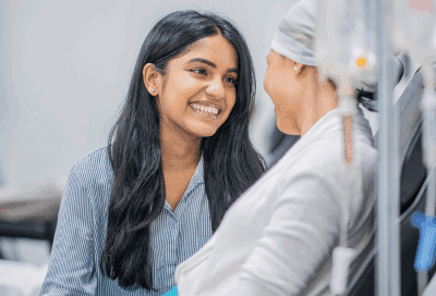 A woman smiling at another woman getting chemotherapy, representing cancer treatment side effects